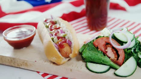 perrito caliente, salsa y ensalada servidos en una tabla de madera