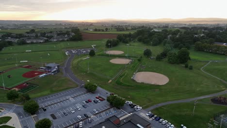 Aerial flyover American high school building with several baseball fields in background. Parking cars on lot. Foggy sunrise in the morning. Ephrata, Pennsylvania. Wide shot