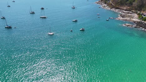 drone footage captures boats anchored in turquoise waters off cape promthep, phuket, showcasing serene coastal beauty and vibrant marine life