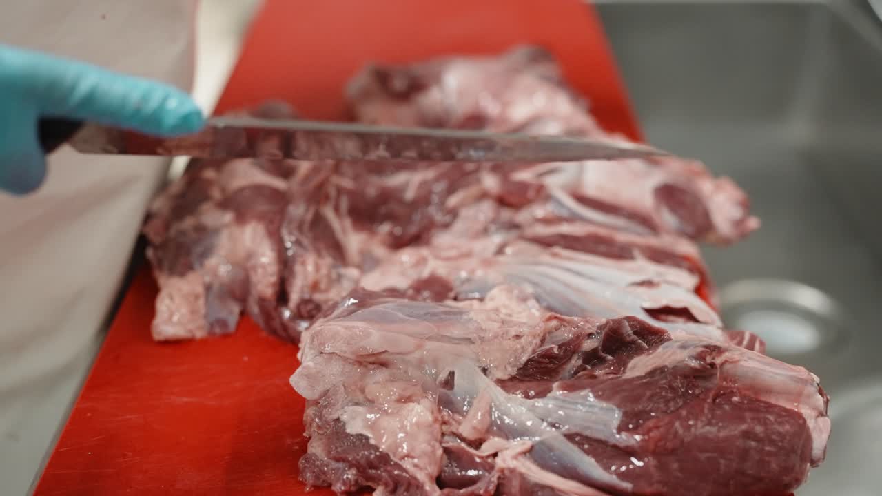 Gloved hands trimming membrane from raw pork meat on cutting board