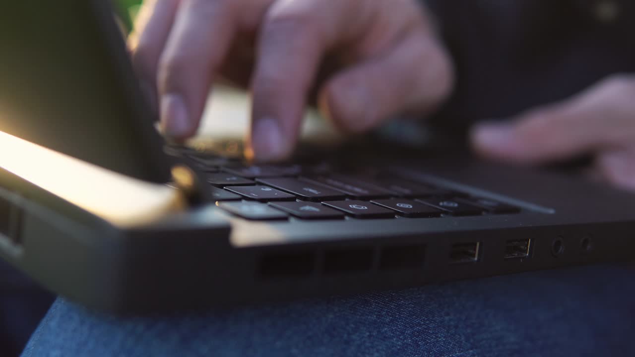 cerca de las manos del hombre escribiendo en el teclado de la computadora portátil durante una hermosa puesta de sol.