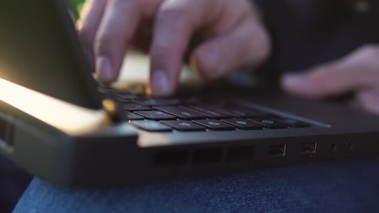 Close up of man's hands typing on laptop's keyboard during beautiful sunset.