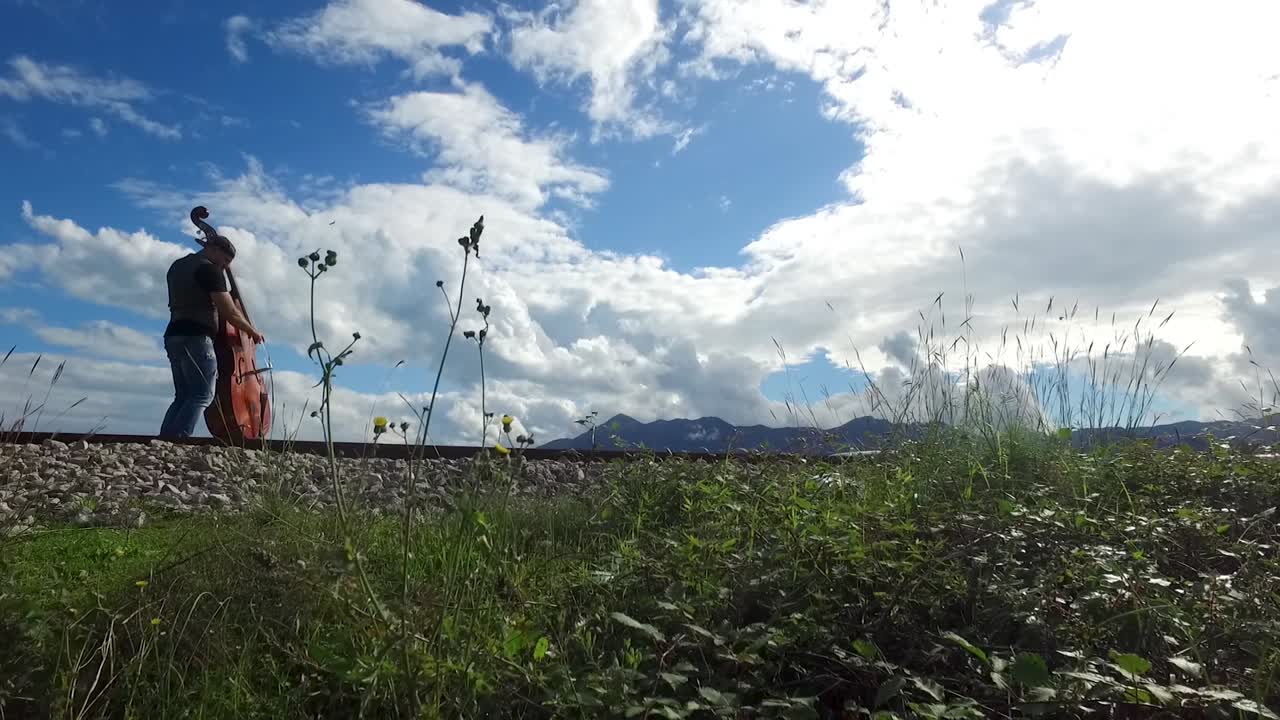 철도 트랙 을 따라 더블 베이스 를 들고 고 있는 사람