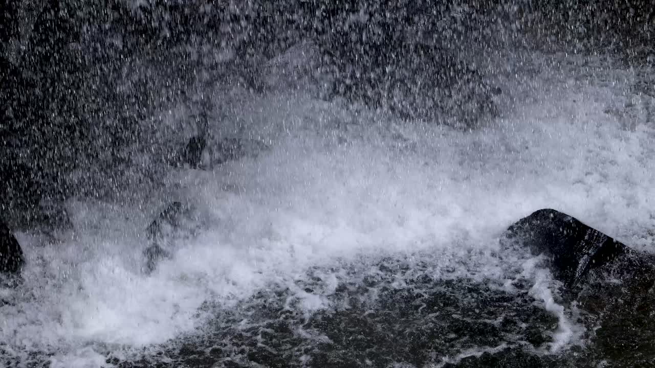 Dynamic close-up of waterfall water forcefully splashing onto dark rocks, captured with natural lighting and a steady camera in Dorrigo, Australia