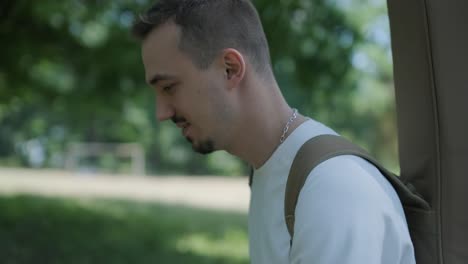 young man walking with guitar on street near forest