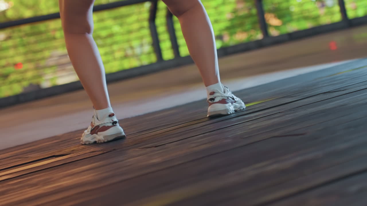 Closeup black woman sneaker footwork on wooden deck, dynamic steps and toe work with textured sole details, lightweight sneakers and agile stance capture athletic rhythm, green park backdrop
