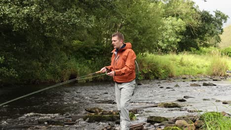 Hand-held-shot-of-a-fly-fisherman-casting-his-line-into-a-small-stream