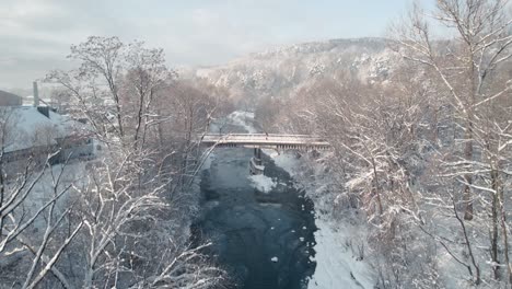 Small-bridge-in-forest-covered-by-snow-and-frozen-river-in-frosty-morning