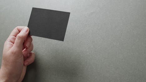 hand of caucasian woman holding black business card on grey background, copy space, slow motion