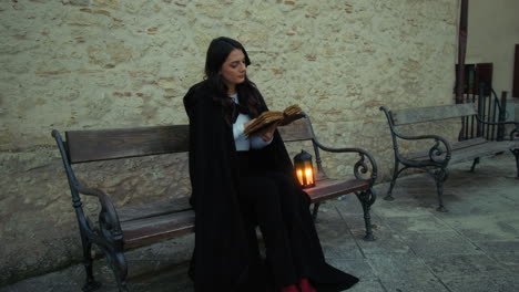 mysterious woman reads a magic book sitting on the square in the city at night