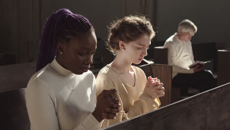 two multiethnic women praying heartily in church