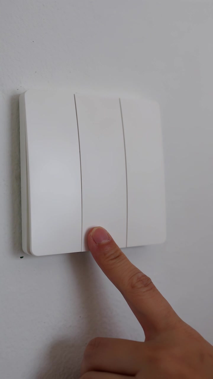 A close-up shot shows a finger pressing a white light switch on a wall