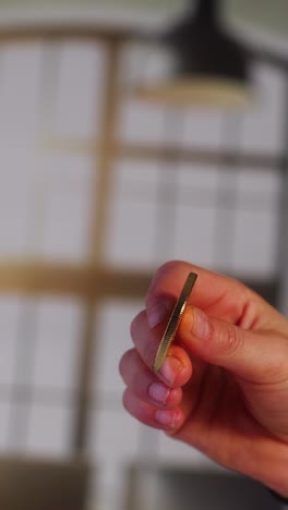a close-up shot of a hand holding a shiny gold-colored bitcoin coin, showcasing the cryptocurrency symbol and detailed engravings, with a soft focus background of interior window panels.