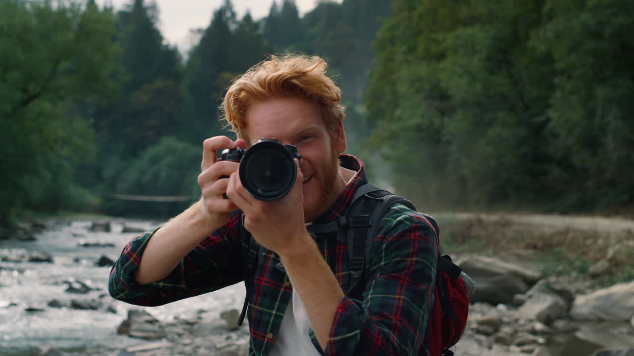 Happy guy with camera standing at river. Photographer taking photos on camera