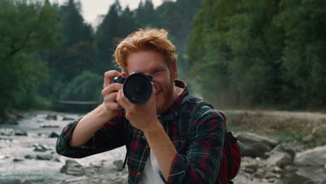 Happy-guy-with-camera-standing-at-river.-Photographer-taking-photos-on-camera