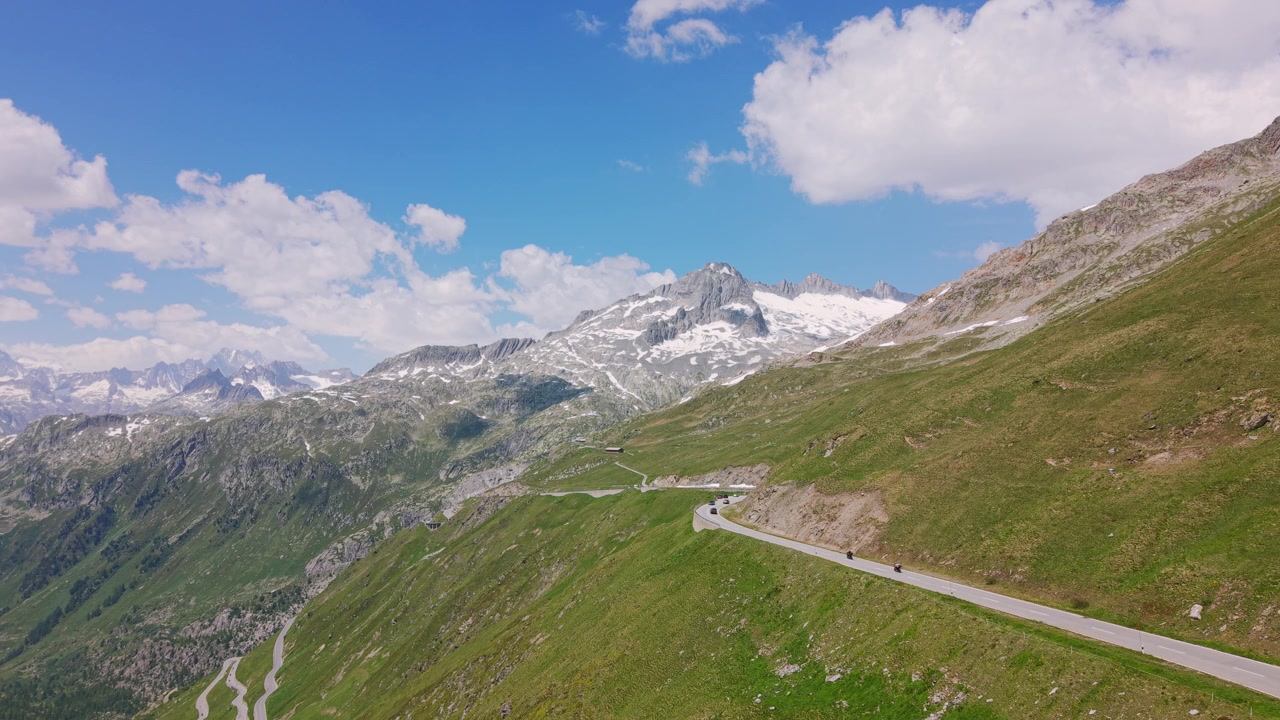 Auto percorrono una tortuosa strada di montagna svizzera sotto un cielo estivo azzurro brillante
