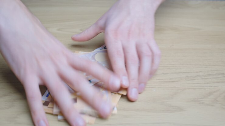 Male hands piling up a lot of paper money bills on a wooden table