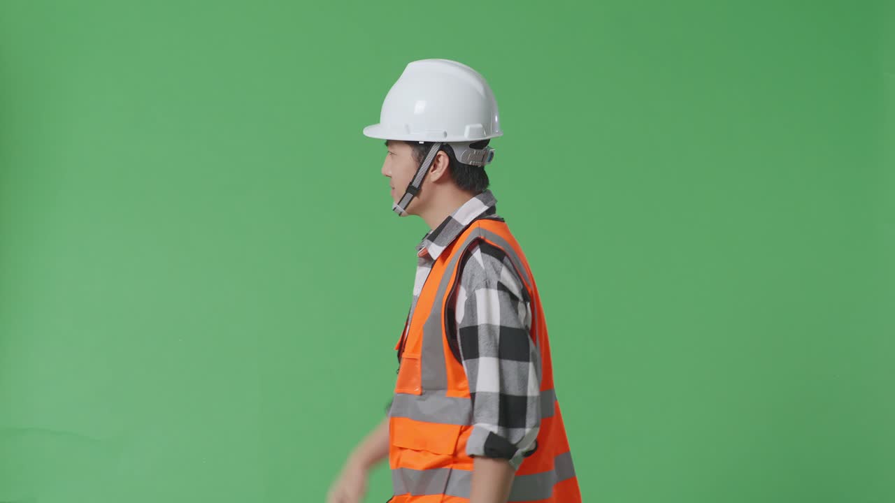안전 헬을 입은 아시아 남성 엔지니어가 녹색 스크린 배경 스튜디오에서 는 동안 손을 흔들고 있는 측면 시각