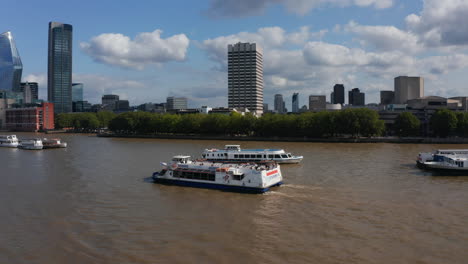 Tracking-shot-of-cruise-ship-floating-on-wide-water-surface-of-River-Thames.-One-Blackfriars-and-skyscrapers-in-City-financial-hub-in-background.-London,-UK