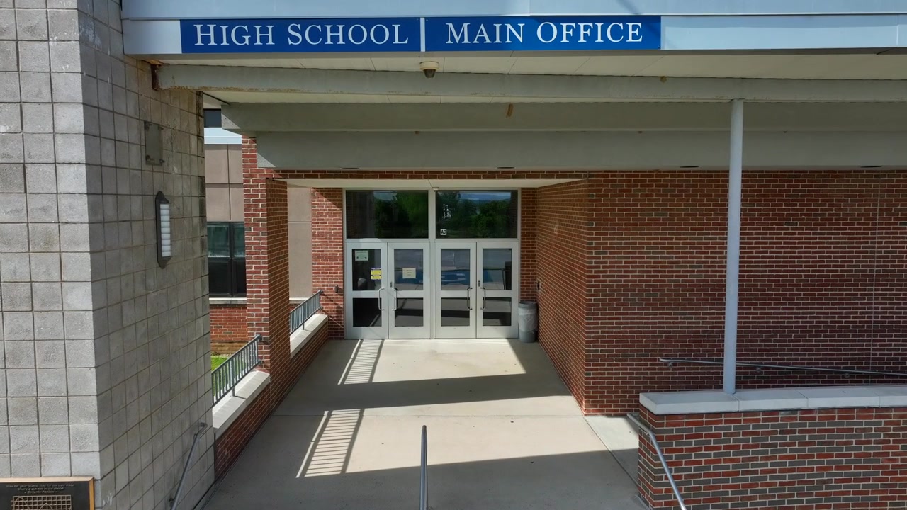 Aerial push in of main office entrance at American in school. High School, Main Office, visitors sign.