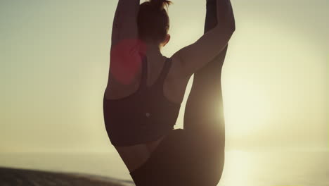 slim girl practicing splits yoga pose with one leg rising up outdoors close up.