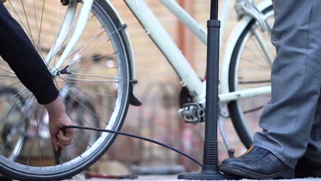 caucasian men fill front tire of white bicycle with air using hand pump, close up static