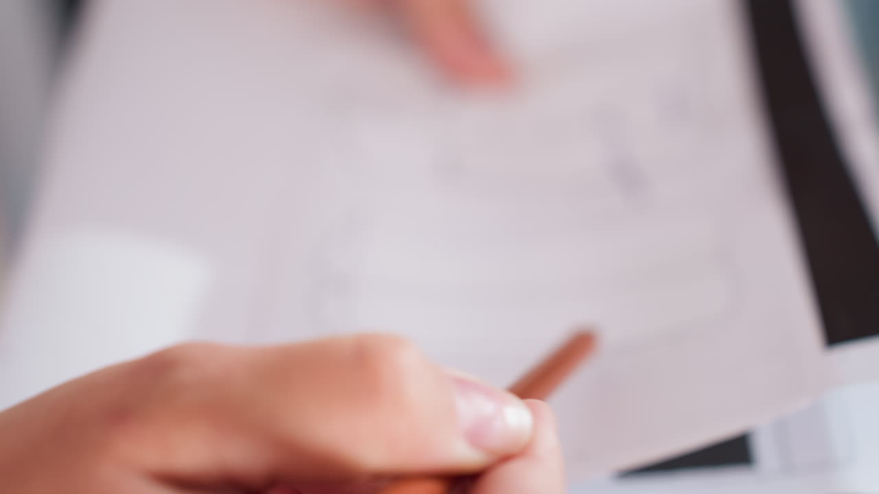 Closeup view of seamstress making precise markings on jacket design sketch using brown pencil while assistant hand points at specific section during fashion project collaboration session indoors