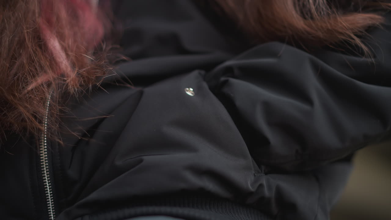 Young person adjusts sleeve during rain outdoors. Student in city adjusting jacket sleeve under rainy sky. Young individual makes sleeve adjustments on their jacket while standing in rainy city street