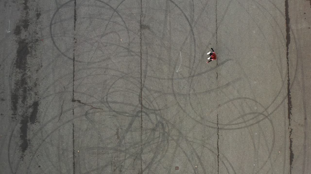 vista aérea de pájaro de una chica patinadora montando patines sobre asfalto, tiro de drones de arriba hacia abajo