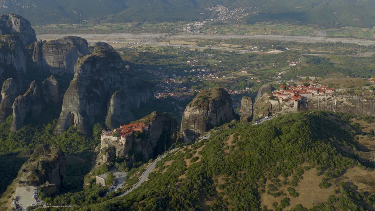 Cinematic aerial view of Meteora monastery in Greece perched on towering cliffs, dramatic rock formations and lush green valley create a breathtaking historic scene