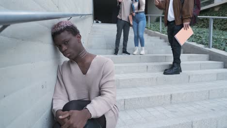 sad african transgender person sitting while a group of students pointing to him