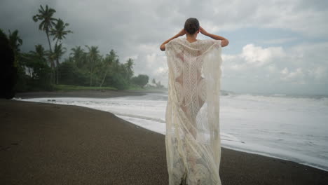 moody tiro amplio de mujer joven e independiente corriendo en la playa de arena negra en bali, indonesia