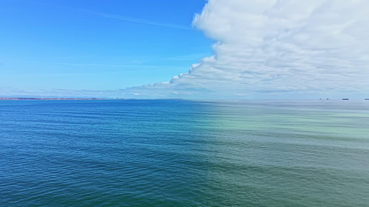 Acqua limpida e blu incontra un cielo nuvoloso all'orizzonte, con navi in lontananza durante il giorno sull'oceano.