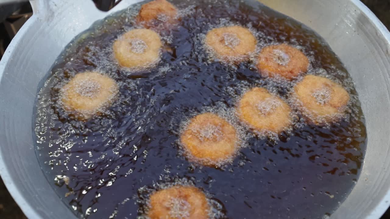SLO MO: Street food vendor cooking and flipping deep fried shrimp cakes or Tod Mun Kung with spatula in boiling hot oil in big wok at local market in Thailand