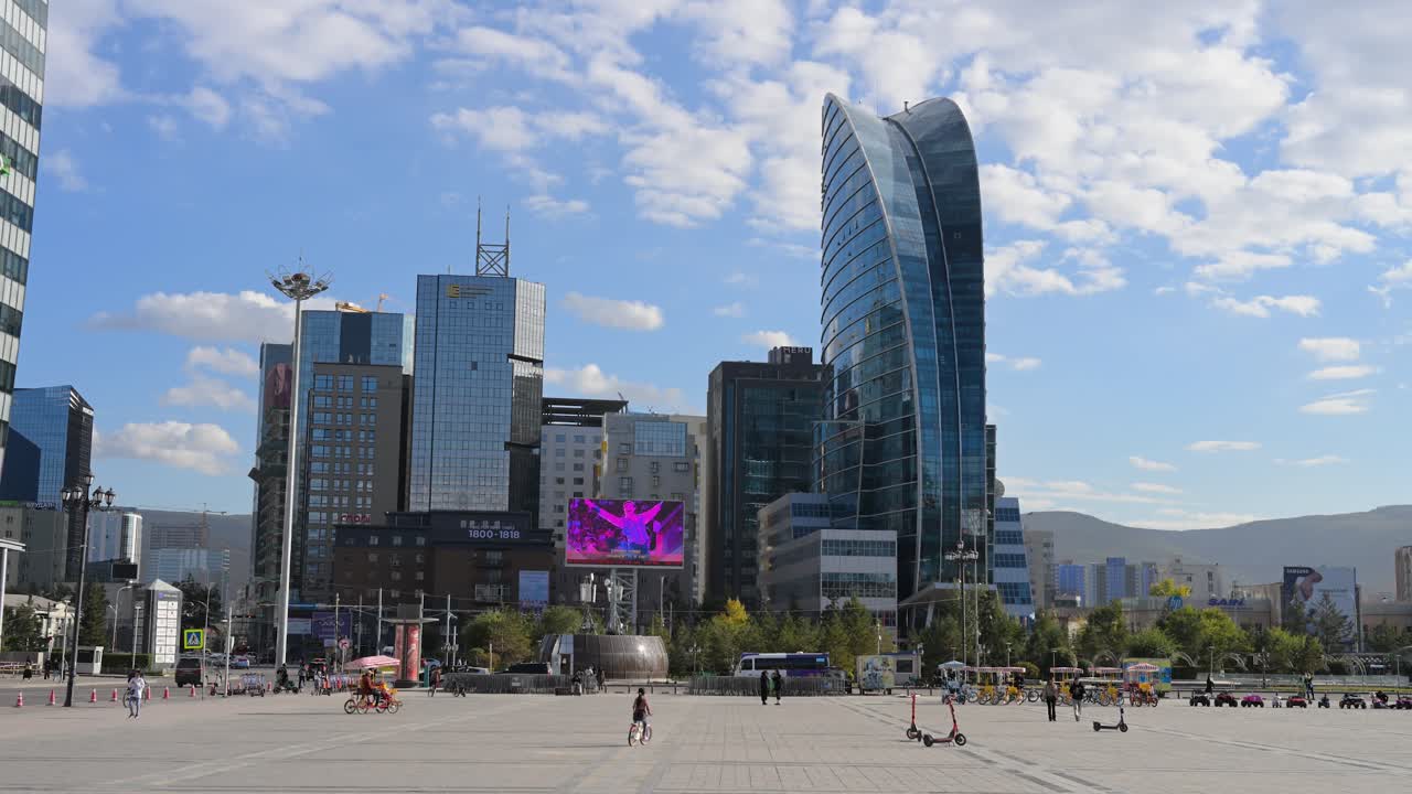 Sunny day view of Sukhbaatar Square, with the Damdin Sukhbaatar statue and modern structures, including the Blue Sky building, visible in the background in Ulaanbaatar, Mongolia.