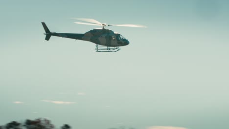 wide shot of a helicopter flying against a blue sky and forested background