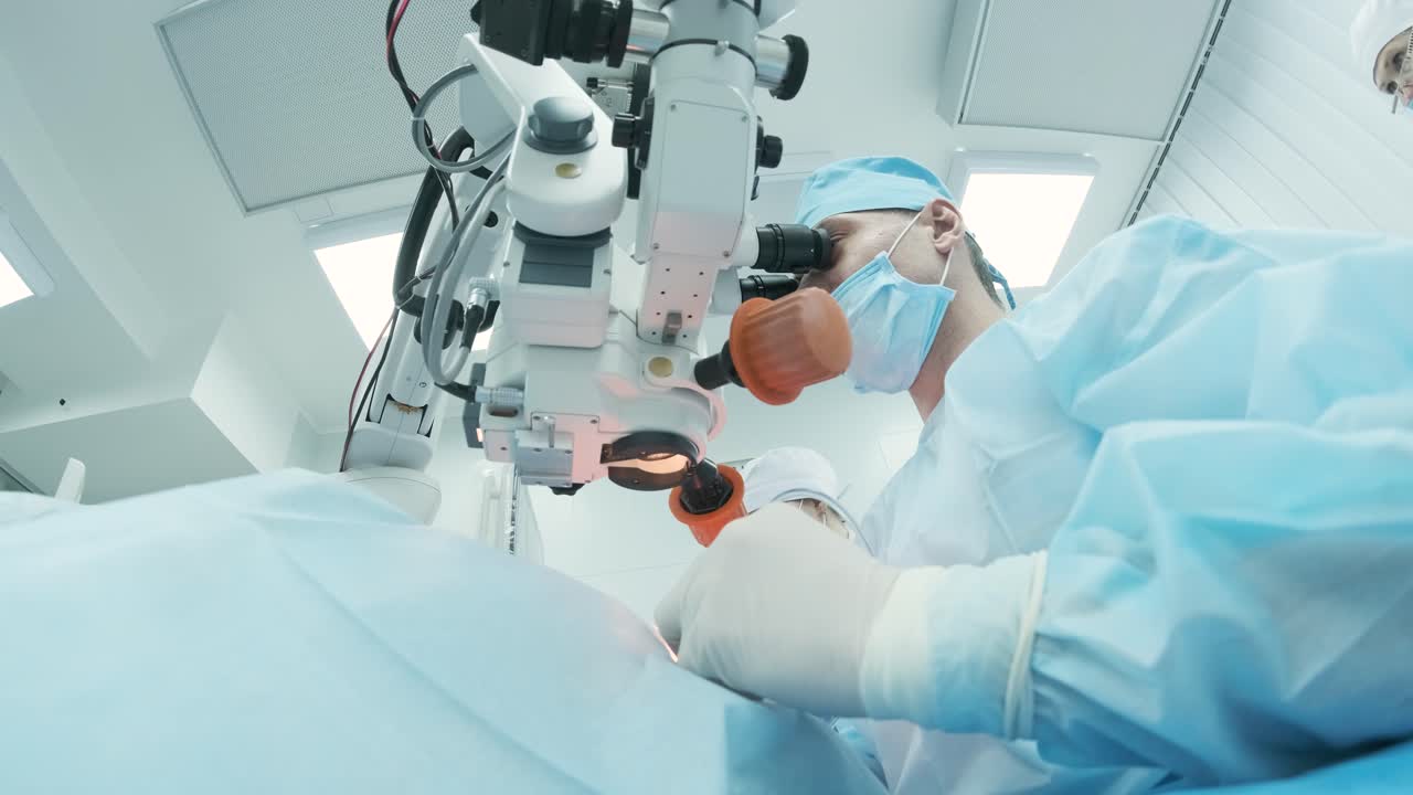 Surgeon looking into the microscope at the eye of female patient at the operating room. Doctor using microscope during eye surgery process, treatment of cataract and diopter correction.