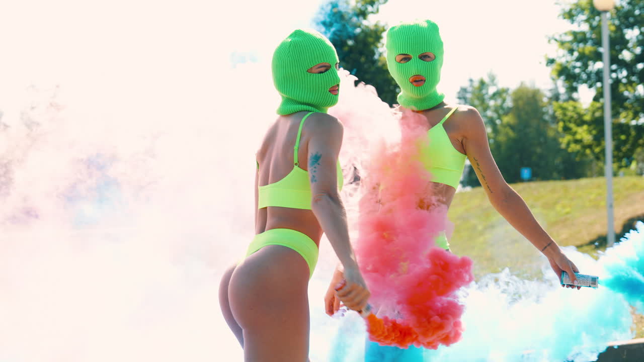 Donne in costumi da bagno verde lime con maschere e fumo colorato