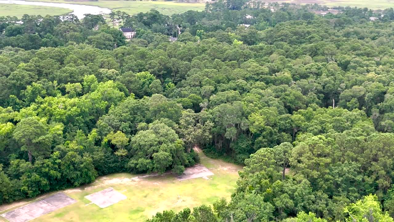 Drone descent from high altitude to grassy clearing in Wilmington Island Reserve; lush green trees fill frame, minimal sky, smooth slide to pilot’s launch spot.