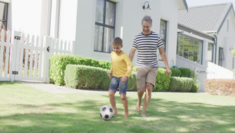 Glücklicher-Kaukasischer-Großvater-Und-Enkel-Spielen-Fußball-Im-Garten,-Zeitlupe