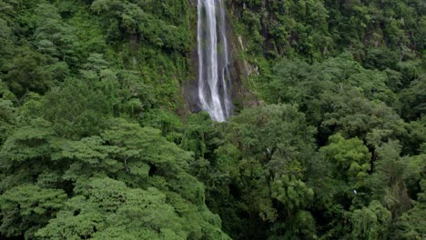 Aerial-rising-over-Las-Lajas-misty-waterfall-falling-into-rocky-pond-surrounded-by-dense-green-woods,-San-Luis-Morete,-Costa-Rica