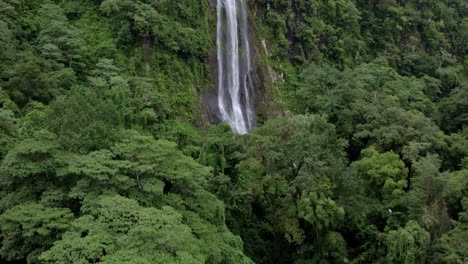 aerial rising over las lajas misty waterfall falling into rocky pond surrounded by dense green woods, san luis morete, costa rica