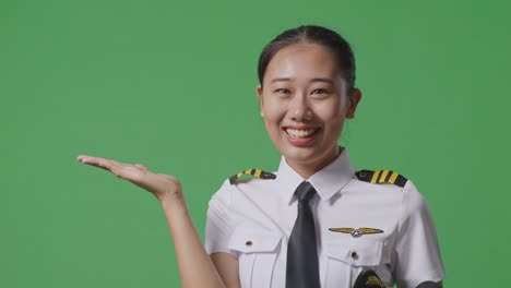 close up of asian woman pilot smiling and pointing to side while standing in the green screen background studio