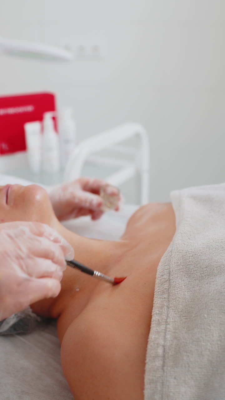 Enzyme therapy cosmetologist applying moisturizing medical cream on young woman chest with brush