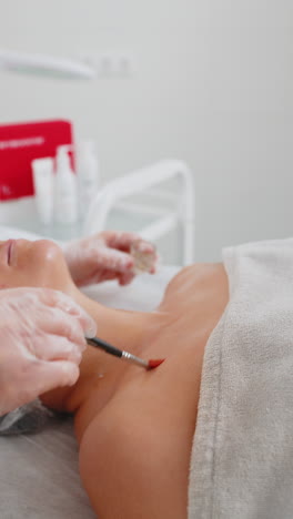 enzyme therapy cosmetologist applying moisturizing medical cream on young woman chest with brush