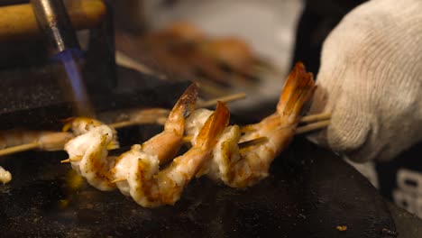 close-up of prawns being flame-torched on skewers, showcasing intense grilling technique.
