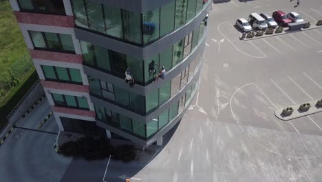 Slow-pull-back-aerial-above-industrial-climbers-hanging-to-clean-office-building-windows