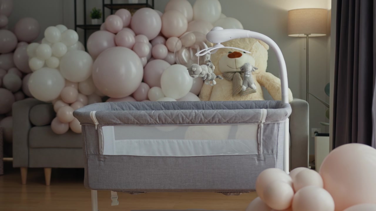 Allestimento di cameretta dai toni neutri con culla, grande orsetto di peluche e decorazioni con palloncini per un baby shower