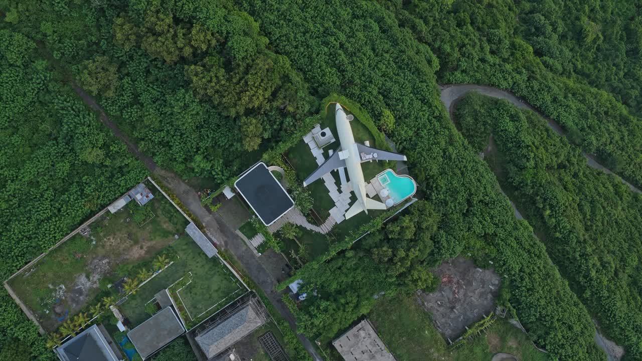 Aerial view of a unique luxury villa made from a repurposed airplane fuselage, complete with a swimming pool on the wing, in bali
