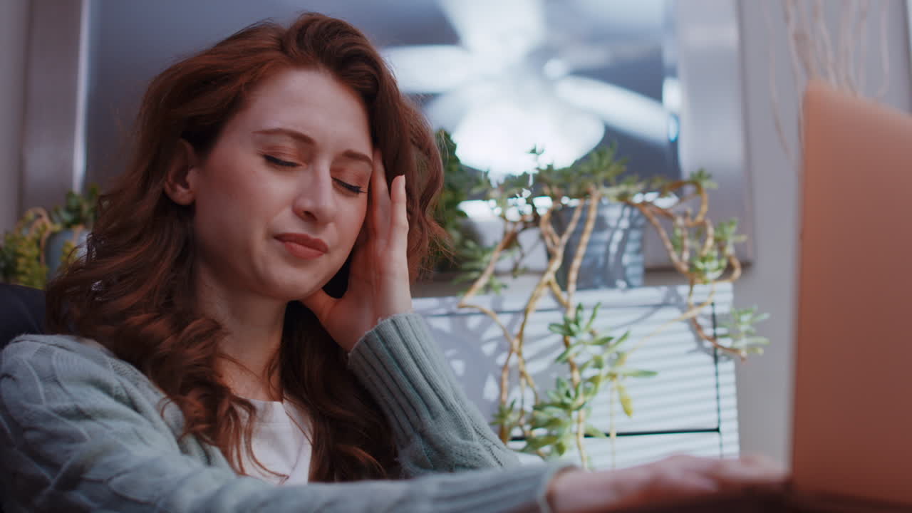 젊은 백인 여성이 노트북으로 집에서 일하면서 두통을 느끼기 시작합니다.